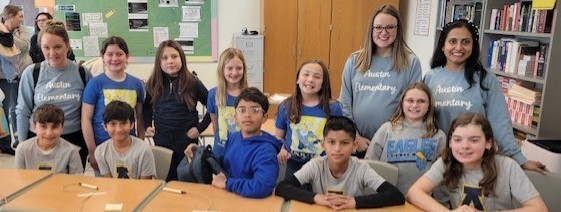 2 adults and students sitting in desks.